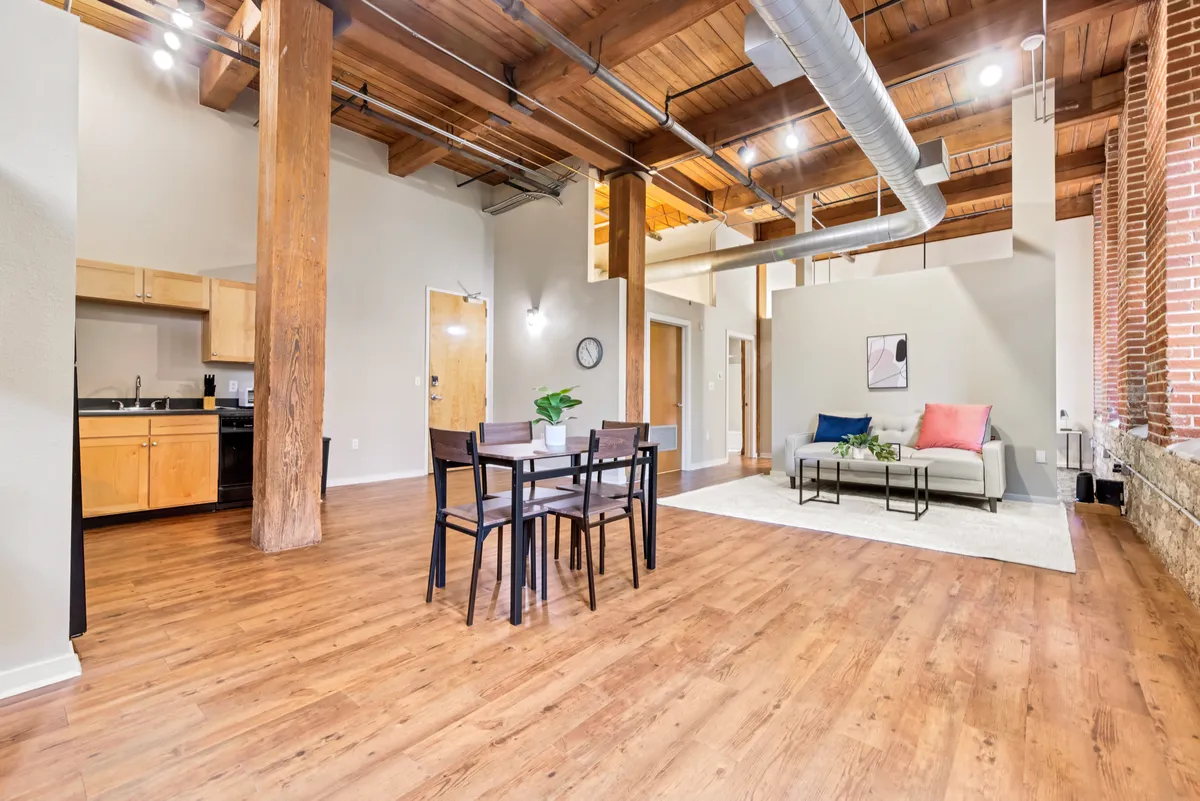 A comfortable, contemporary living and dining area with a dining table and chairs, a plush sofa with colorful pillows, and a nearby kitchen. The setup is inviting for both social gatherings and quiet nights in, with ample room for friends or family.