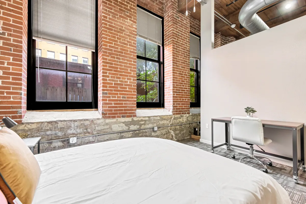 A sunlit interior space with exposed brick walls, large windows, and a minimalist desk near the window. While this is not a kitchen, the historic brickwork and overall warmth of the space evoke the blend of heritage and modern design discussed in the section.