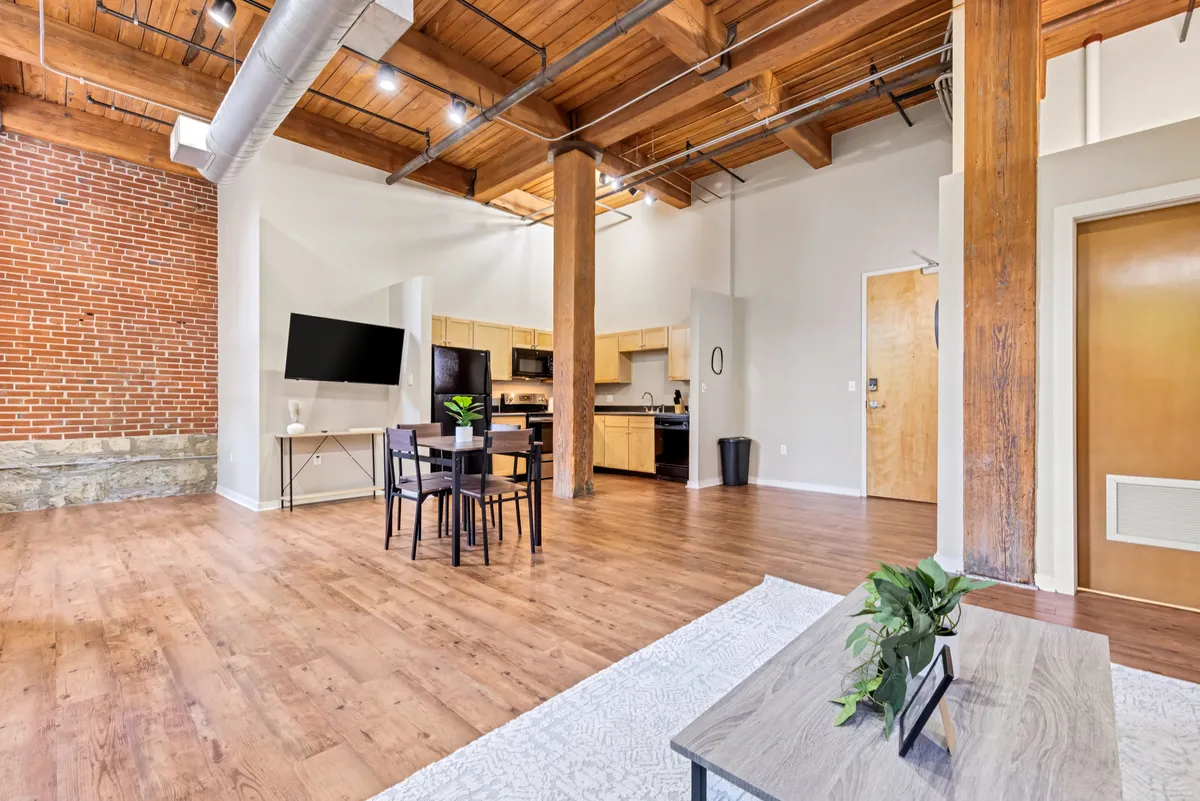 A stylish dining space with a prominent exposed brick wall, rustic wooden beams, a modern dining table, and a television, blending classic architectural details with contemporary living features.